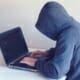 A hacker working on their laptop with a hoodie on, one of the reasons you need to know Threat Intelligence and how it can help you.